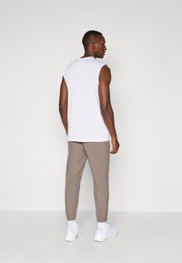Hvid ærmeløs top og lysebrune tapered bukser. Bukserne har elastiske manchetter, og outfittet er parret med hvide sneakers.