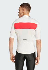 Jersey de ciclismo blanco con una amplia franja horizontal roja, de mangas cortas y ajuste ceñido. Combinado con pantalones cortos de ciclismo negros que cuentan con un panel acolchado.