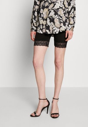 Shorts noirs avec une bordure en dentelle au bas, portés avec un blouse à motifs floraux et des talons noirs à lanières.