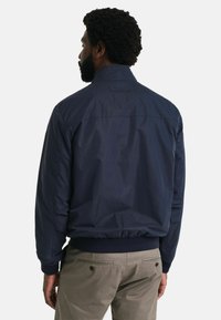 Navyblauwe bomberjack met ribbels bij de manchetten en tailleband, met een gladde, matte afwerking en een eenvoudig kraagontwerp.