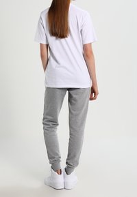 White cotton t-shirt, relaxed fit, paired with gray sweatpants. Model wears white shoes. Simple design with no visible patterns or hardware.