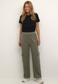 T-shirt noir associé à un pantalon cargo loose vert olive avec des poches latérales et une coupe décontractée, complété par des chaussures de sport légères.