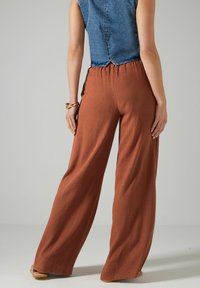 Spodnie o szerokich nogawkach w kolorze rdzy, wykonane z lekkiego materiału. Elastyczny pas, z luźnym krojem, zestawione z dżinsowym topem bez rękawów.