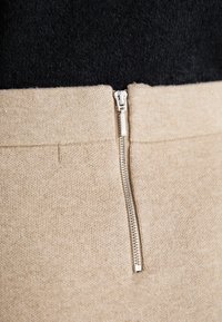 Beige színű pulóver, cipzáros záródással, puha kötött anyagból készült. Texturált felülettel és fekete felső résszel rendelkezik.