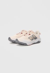 Une paire de baskets beige avec des semelles grises et un logo noir, positionnée côte à côte sur un fond blanc uni.