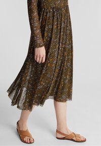 Brun mönstrad klänning med långa ärmar och vid kjol, tillsammans med tanfärgade sandaler med remmar. Har blommiga och geometriska mönster.