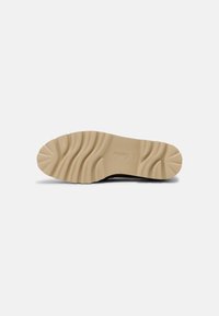 Suela negra de zapato con una suela exterior de goma beige texturizada, que presenta ranuras curvas y un logo estampado para el agarre y la estabilidad.