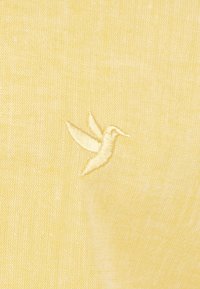 Gelber Stoff mit einer strukturierten Webart, die ein dezentes gesticktes Kolibri-Muster in einem etwas helleren Gelbton zeigt.