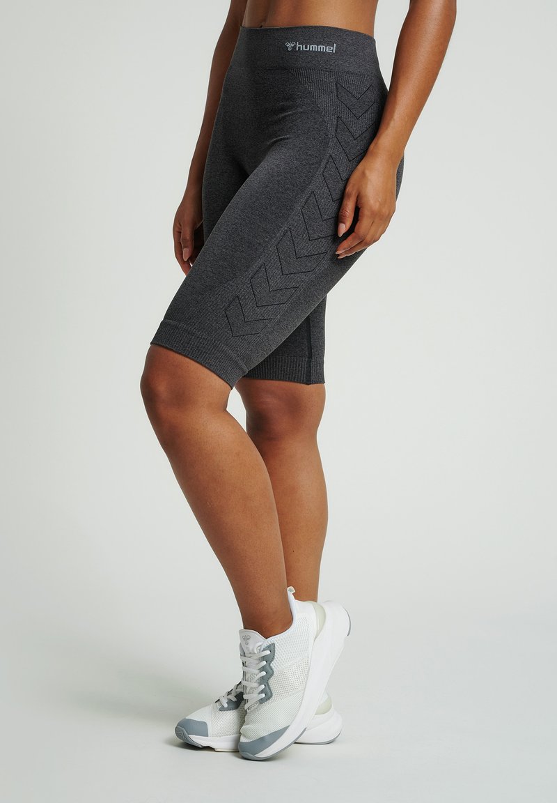 Gray stretchy cycling shorts with a high waistband. Side pattern features raised chevrons. Paired with white and gray athletic shoes.