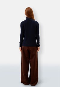 Maglione a collo alto lavorato a maglia di colore navy con maniche lunghe, abbinato a pantaloni larghi marroni. Tessuto morbido e silhouette aderente.