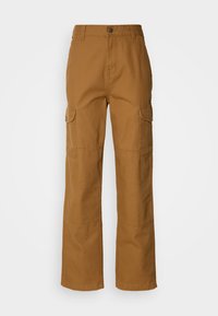 Liikudhousut ruskeasta puuvillakankaasta, jossa on leveä lahkeenosuus, kaksi sivutaskua ja näkyviä ompelutakkeja.