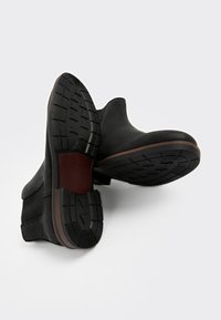 Sorte ankelstøvler med en glat læderoverdel, gummisål med mønstret slidbane og en kontrasterende brun detalje ved mellemsålen.