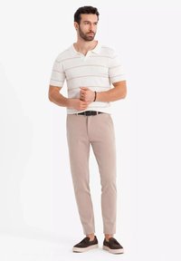 Bílý polo s krátkým rukávem a jemnými pruhy, béžové slim-fit kalhoty a tmavé tenisky, se límečkem a jemnou texturou.