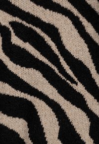 Stickad tyg med ett zebramönster i svart och beige, med en mjuk textur och kontrasterande färger.