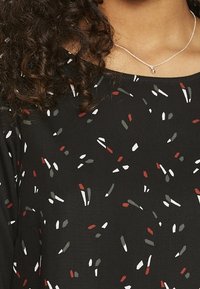 Czarna bluzka z rozproszonym wzorem czerwonych, białych i zielonych kształtów. Gładki materiał, okrągły dekolt i krótkie rękawy.