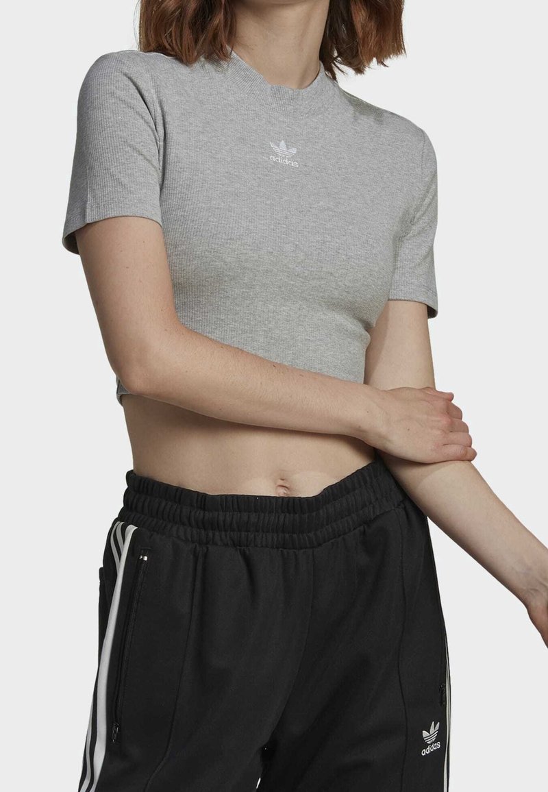 Grå ribbad cropped t-shirt med korta ärmar, med en vit Adidas-logga på bröstet, ihop med svarta joggers med elastisk midja.