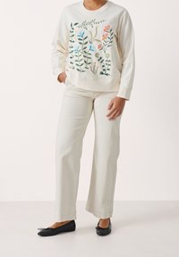 Sweat-shirt couleur crème avec broderie florale en bleu, rose et vert, associé à un pantalon large de couleur claire et des ballerines noires.