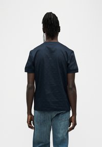 Μπλε ναυτικό βαμβακερό μπλουζάκι με στρογγυλή λαιμόκοψη και κοντά μανίκια, με διακριτική υφή και ευθεία ραφή στο τελείωμα. Συνδυάζεται με ανοιχτόχρωμο τζιν παντελόνι.