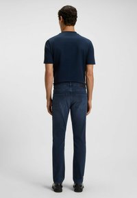 Mörkblå bomullströja med korta ärmar, i kombination med mörkblå slim-fit jeans. Outfitten har subtila sömmar och en standard design på baksidan.