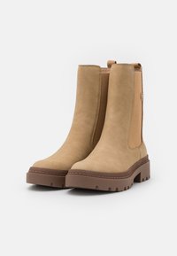 Bottines en suède beige avec panneaux latéraux en élastique, une semelle en caoutchouc marron contrastante et une semelle extérieure épaisse et texturée pour une meilleure adhérence.