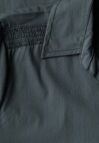 Tessuto grigio scuro con una texture liscia, caratterizzato da un pannello arricciato e un colletto strutturato. Cuciture visibili lungo i bordi.