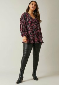 Blomstret bluse i sort, pink og rød med afslappet pasform og rynkede ærmer, parret med sorte læderleggings og hælede støvler.