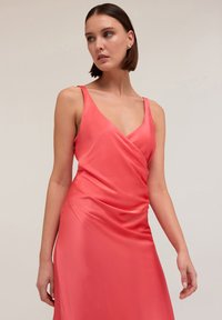 Rochie din satin coral cu decolteu adânc în V, bretele subțiri și un design drapat. Textură netedă cu o siluetă fluidă și hardware minim.