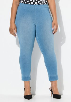 Helle blaue, dehnbare Jeans mit glatter Textur, hoher Taille, schmaler Passform und aufgekrempeltem Saum. Kombiniert mit schwarzen High Heels.