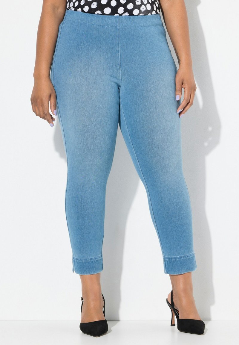 Světle modré, elastické džíny s hladkou texturou, vysokým pasem, slim fit a ohrnutými lemy. Kombinované s černými vysokými podpatky.