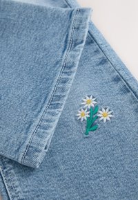 Tissu en denim bleu clair avec un petit motif brodé de trois marguerites blanches aux centres jaunes et aux tiges vertes.