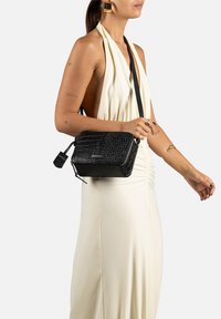 Borsa a tracolla rettangolare nera realizzata in pelle texturizzata con motivo coccodrillo e rifiniture in argento. Caratterizzata da chiusura con zip e spallaccio regolabile.
