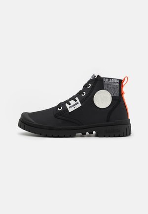 Czarny wysoki sneaker Palladium z białymi naszywkami z logo, czarnymi sznurowadłami, wytrzymałą podeszwą oraz pomarańczową pętelką na pięcie na jednolitym białym tle.