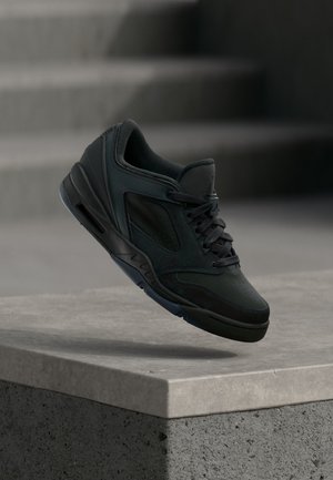 Baskets de sport noires avec lacets, en l'air au-dessus d'un rebord en béton et des escaliers flous en arrière-plan.