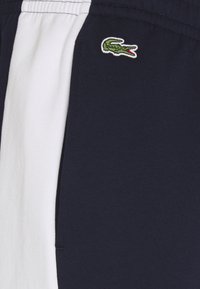 Marina blå träningsshorts med ett vitt band, med en liten grön krokodil-logotyp broderad på sidan. Mjuk tygkänsla.