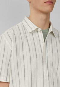Kurzarm gestreiftes Hemd in hellem Creme mit grauen Linien; Button-Down-Kragen; weicher, strukturierter Stoff; mit sichtbarer innenseite.
