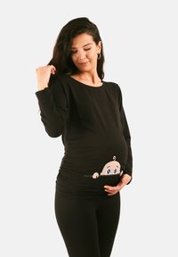 Schwarzes langärmeliges Schwangerschaftsoberteil mit einem Cartoon-Babymotiv im Bauchbereich, runder Halsauschnitt und gerafften Seitennähten.