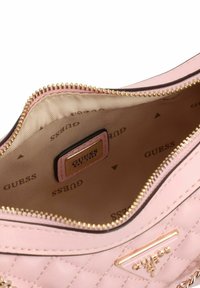 Sac à main matelassé rose avec fermeture à glissière dorée, présentant un intérieur beige avec une étiquette logo. Comprend des accents en quincaillerie brillante.