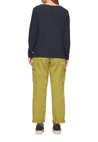 Top de manga larga texturizado en navy combinado con pantalones cargo en verde oliva, que cuentan con grandes bolsillos laterales y puños doblados, usados con zapatillas oscuras.