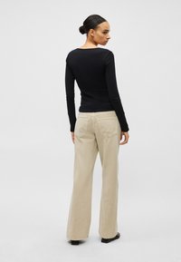 Juodas ilgomis rankovėmis viršus derinamas su smėlio spalvos plačiomis kelnėmis. Viršus turi apvalų kaklo iškirpimą, o kelnės yra tekstūruotos ir turi galines kišenes.