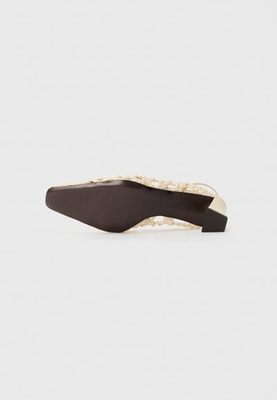 Zapato de tacón alto tejido en color beige con un tacón de bloque negro. Presenta un material texturizado y un diseño abierto. La suela es plana y ligeramente puntiaguda.