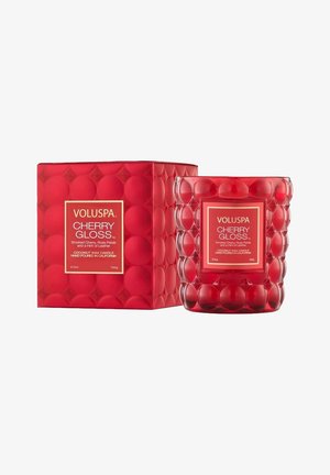 Rød kokosvokskande i tekstureret glas, sekskantet form med afrundede detaljer, mærket "Voluspa Cherry Gloss." Æsken har et matchende design.