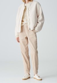 Kurtka z ocieplanym polarem, zapinana na napy, w połączeniu z jasnobeżowymi spodniami z korduroyu i białymi sneakersami. Prosty, teksturowany wzór.