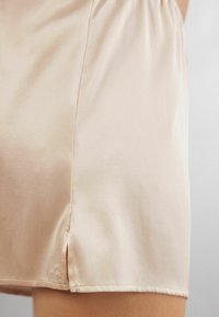 Satinshorts i mjuk beige, med resårmidja, en slät yta och en sidoklaffdetalj vid sidsömmen.