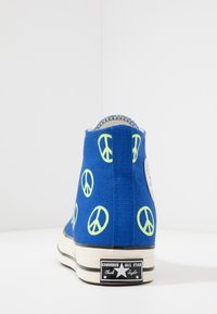 High-top blue canvas sneakers featuring neon peace sign patterns. Black rubber sole with white stripes and Converse branding on the heel.