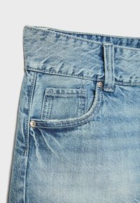 Gros plan sur un jean en denim bleu clair montrant la poche avant, la petite poche à monnaie, la passants de ceinture et les détails des coutures.