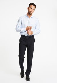 Lichtblauwe blouse met lange mouwen en knoopsluiting, gecombineerd met donkere, op maat gemaakte broeken en zwarte schoenen, met een slim fit en een gladde textuur.