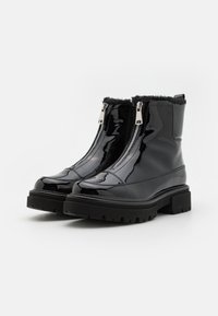 Bottines en cuir verni noir avec double fermeture éclair latérale, doublure en fausse fourrure sur le dessus et semelle en caoutchouc noir épaisse et texturée.