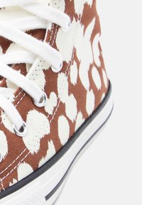 Κοντινό πλάνο ενός ψηλού καμβά αθλητικού παπουτσιού με καφέ και λευκά στίγματα, λευκά κορδόνια και λευκή λαστιχένια σόλα με μαύρο περιθώριο.