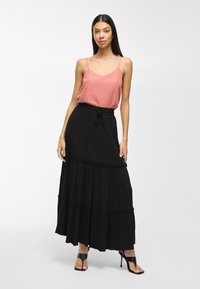 Jupe maxi noire avec un design à volants, des bords finis et une taille à cordon de serrage ajustable, assortie à un débardeur à motifs chevrons roses.