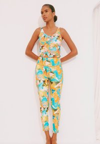 Set format din maiou multicolor și colanți cu modele tropicale, realizat din material elastic. Culorile principale includ galben, albastru și portocaliu.